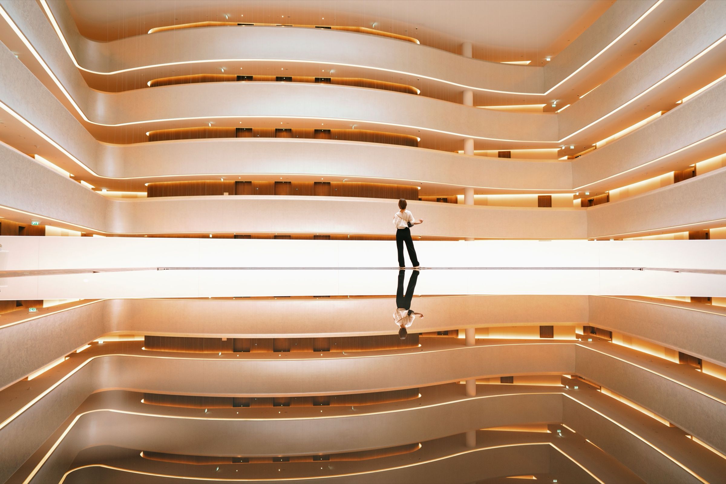 Layered white balconies in warm light, with a single person standing in the centre.