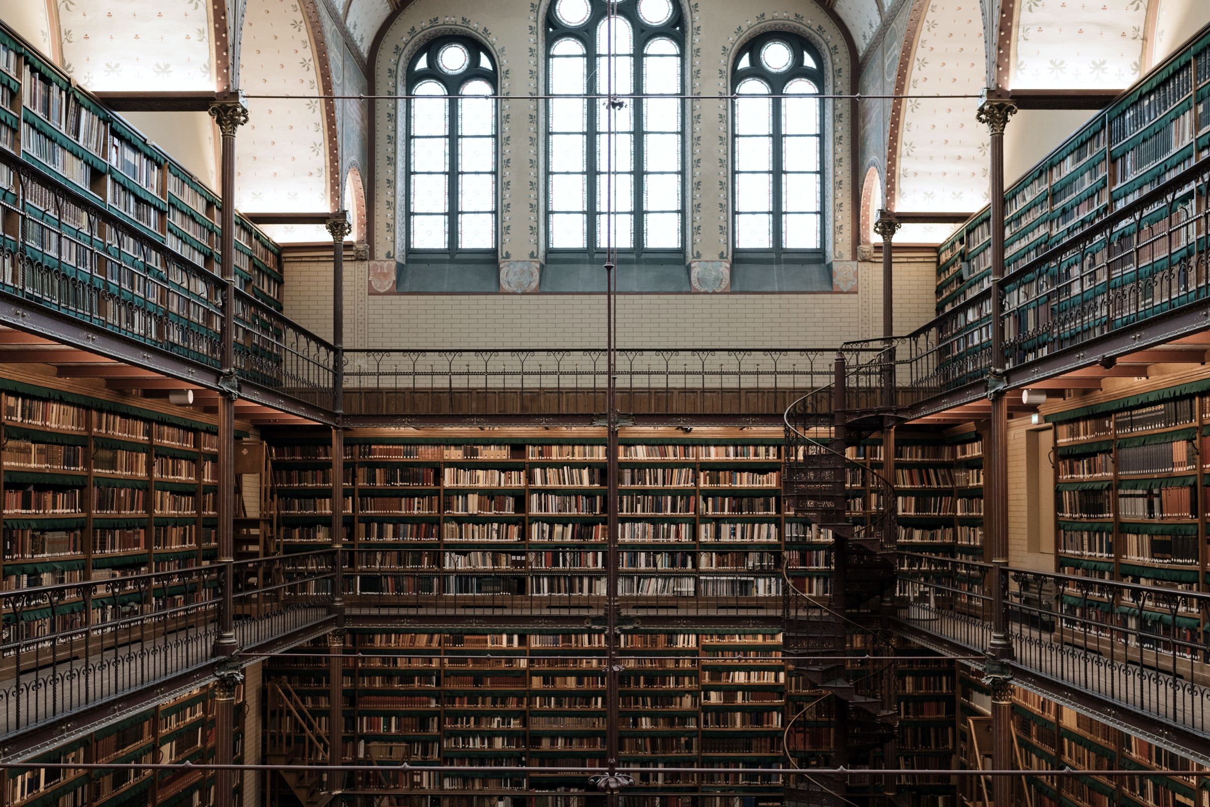A galleried research library under arched windows, a spiral stair in the corner.