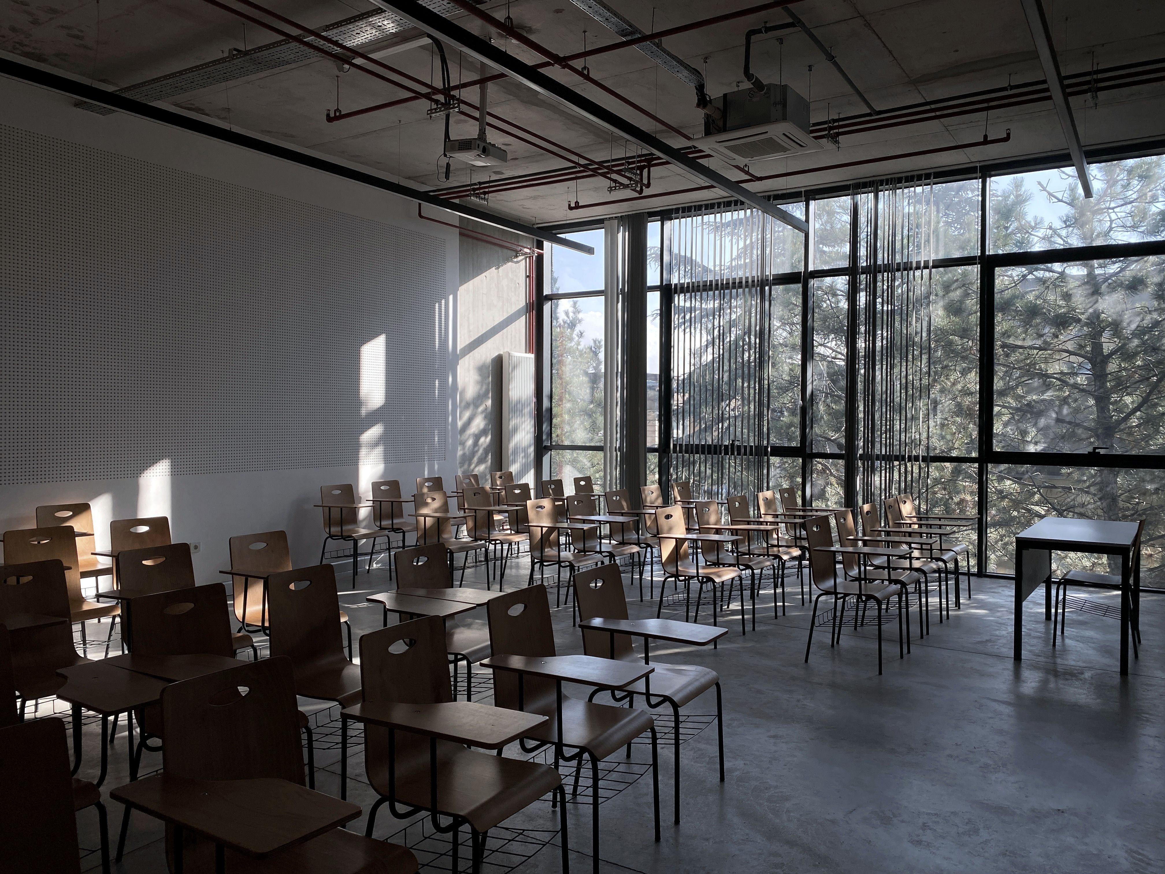 A classroom behind a full-height glazed wall, trees outside and daylight across the desks.