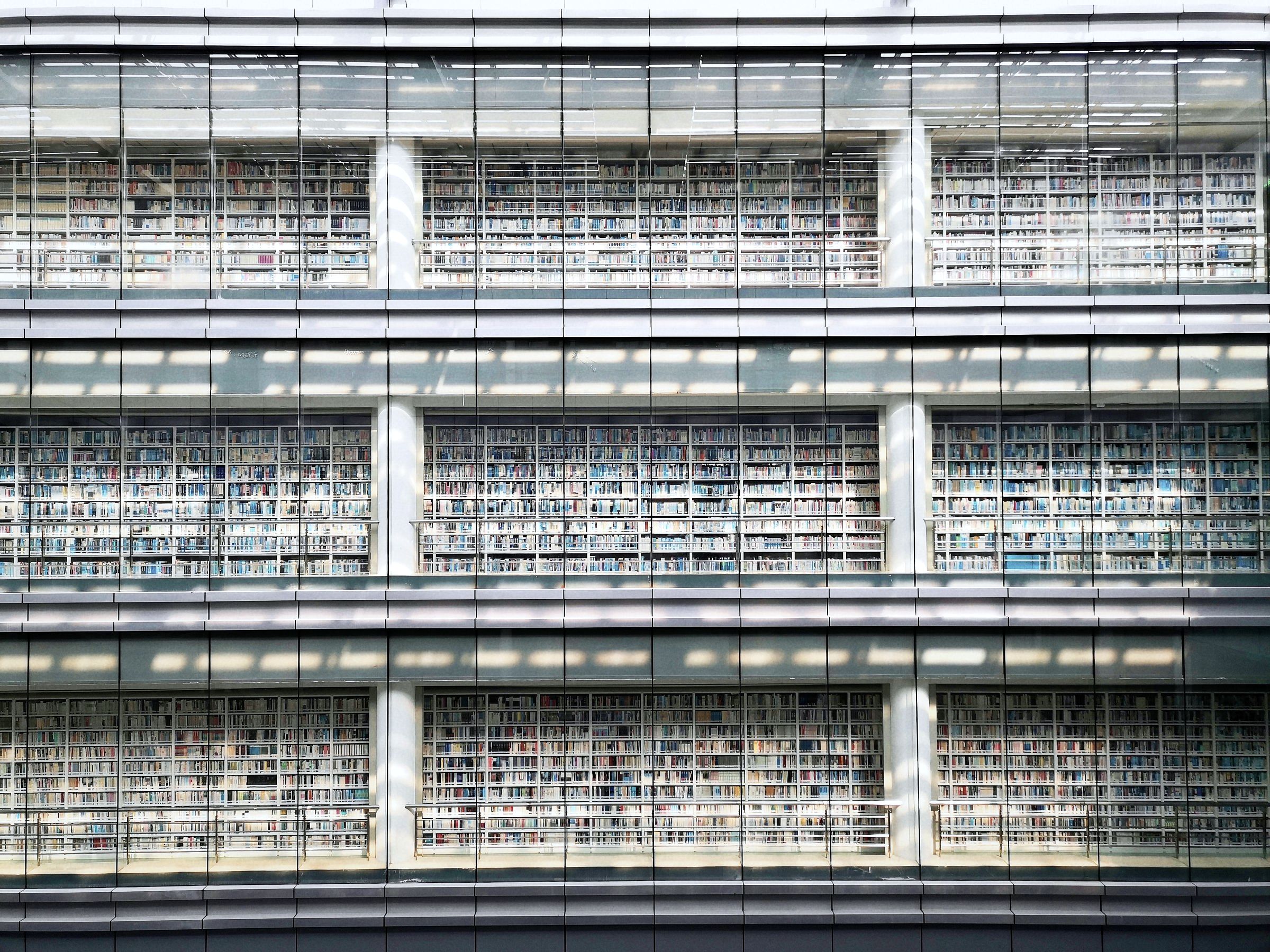 A library seen through its glass facade, three storeys of shelves in daylight.