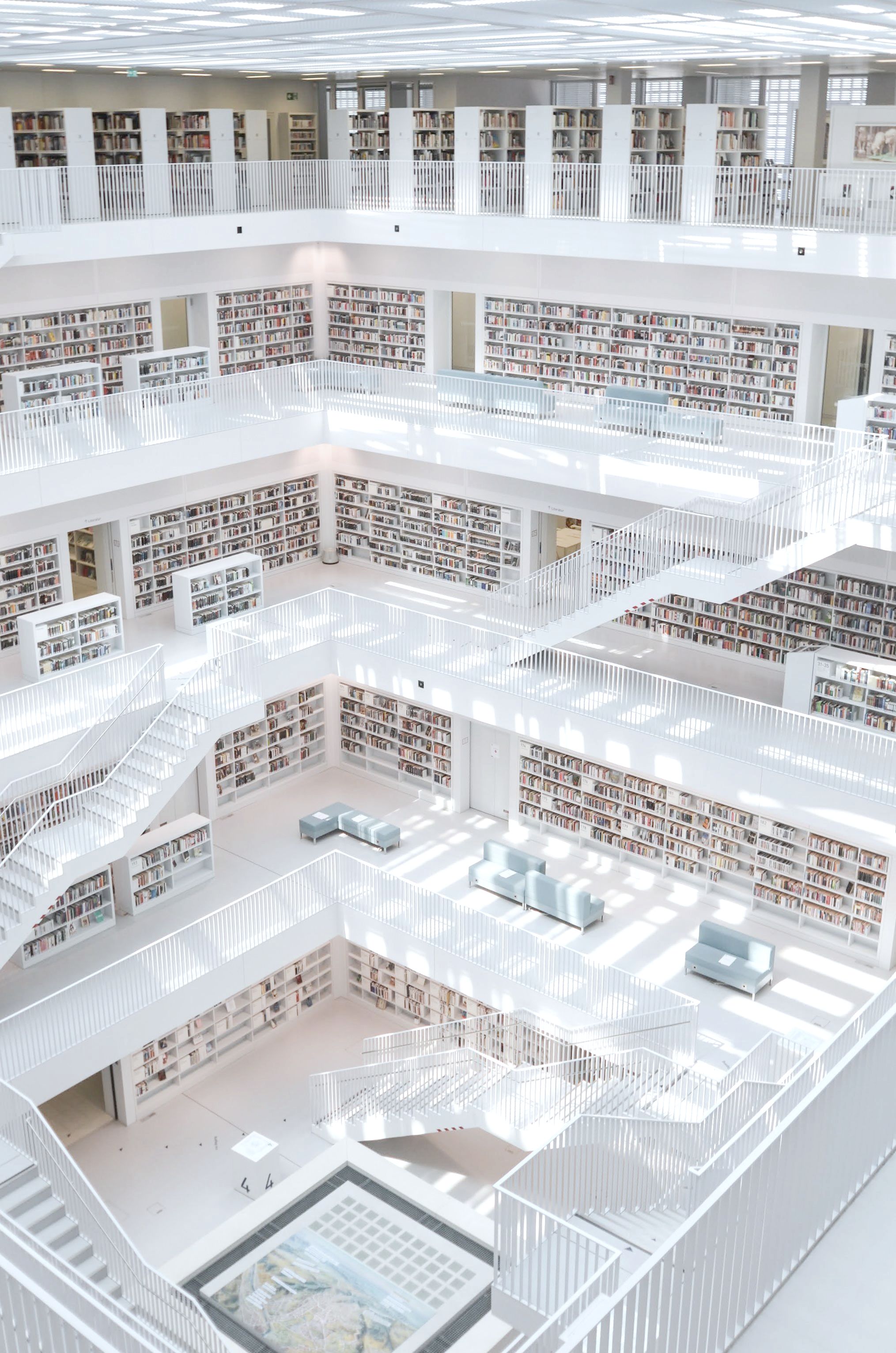 A white library of five galleries around an open well, daylight falling across the shelves.