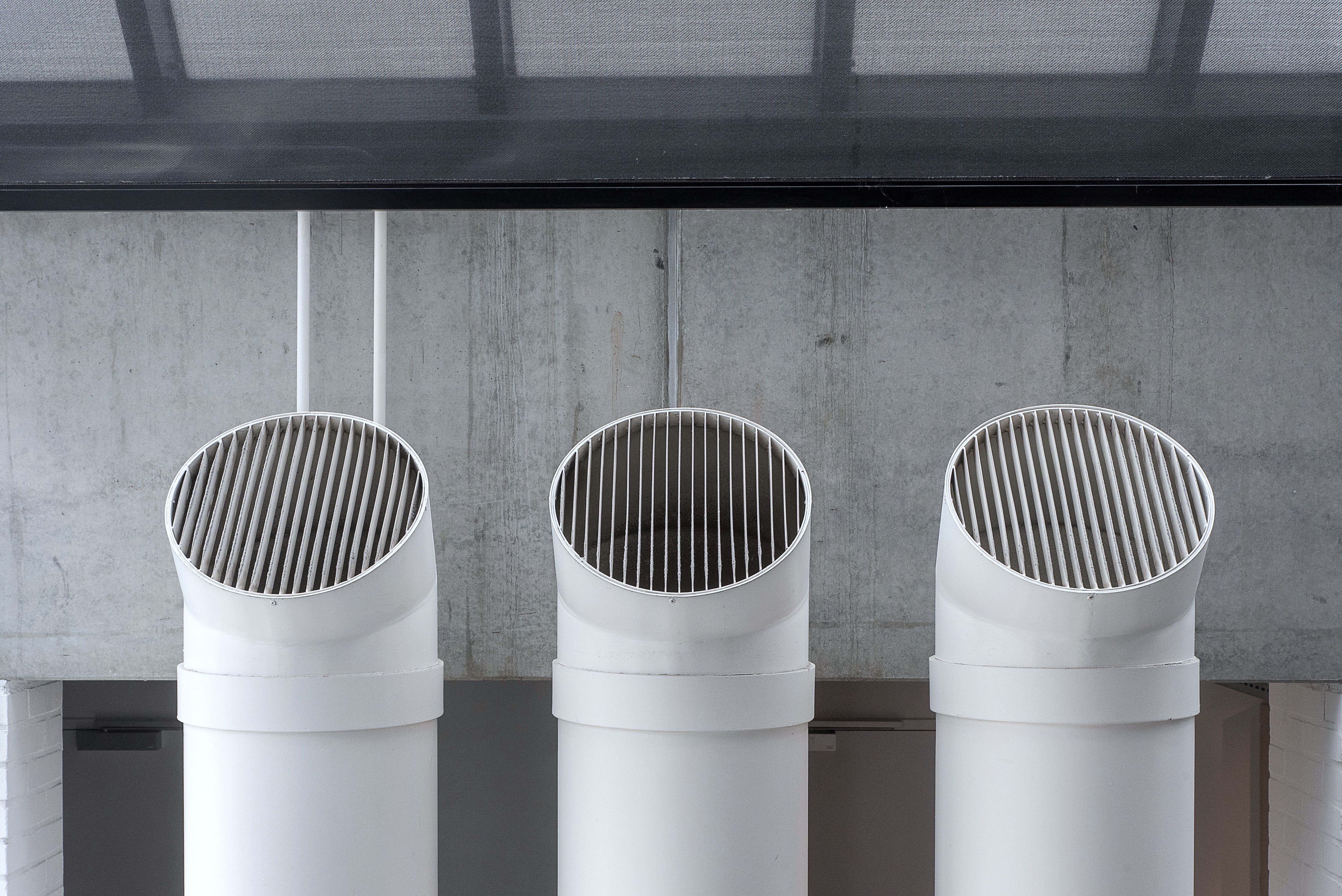 Three white ventilation pipes against a concrete wall.