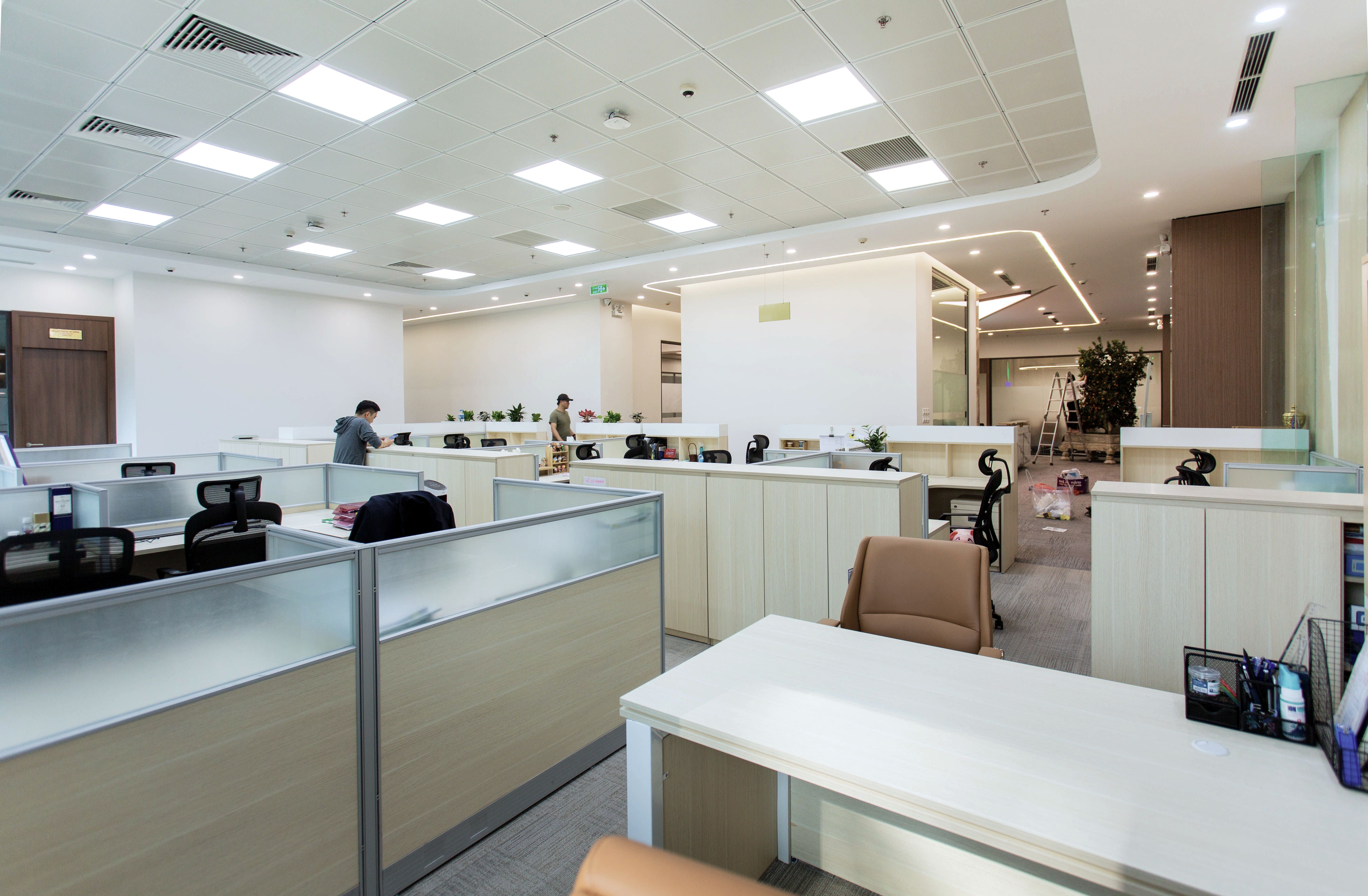 A wide office floor with low partitions, people at desks in the distance under even ceiling light.