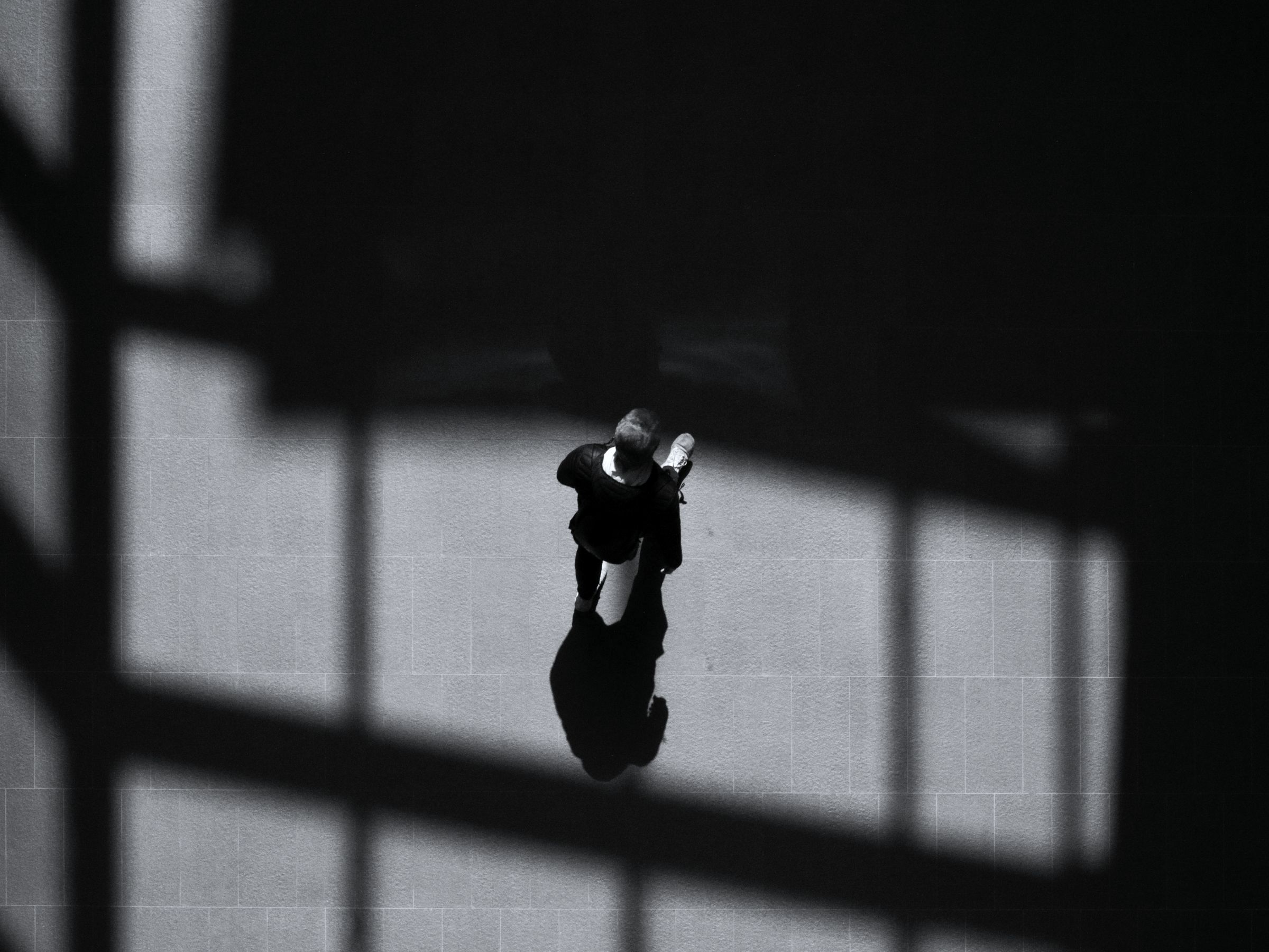 Seen from above, a person crossing a paved square in hard diagonal shadows.