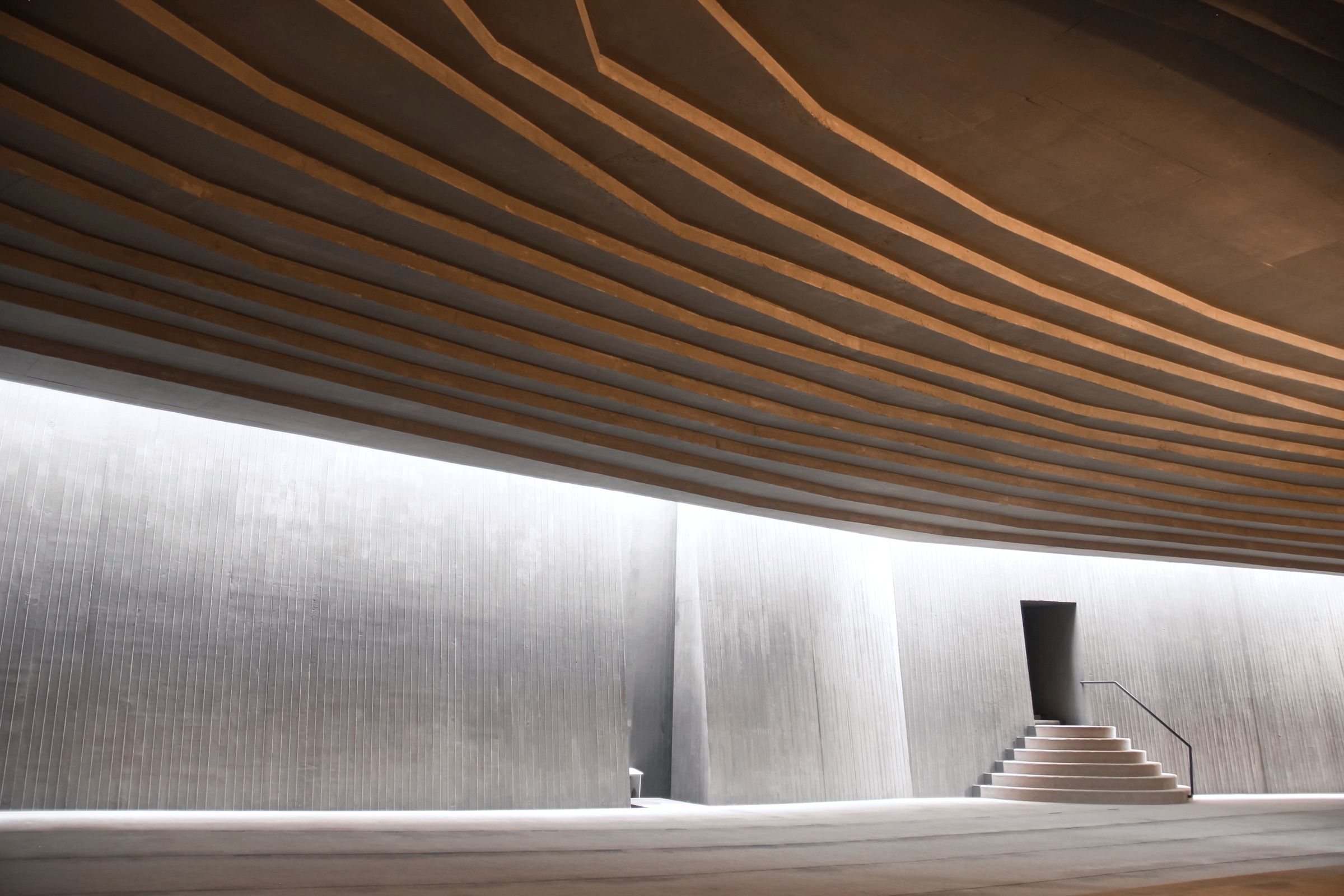 Curved concrete ceiling above a wall with a stair and a doorway, in soft side light.