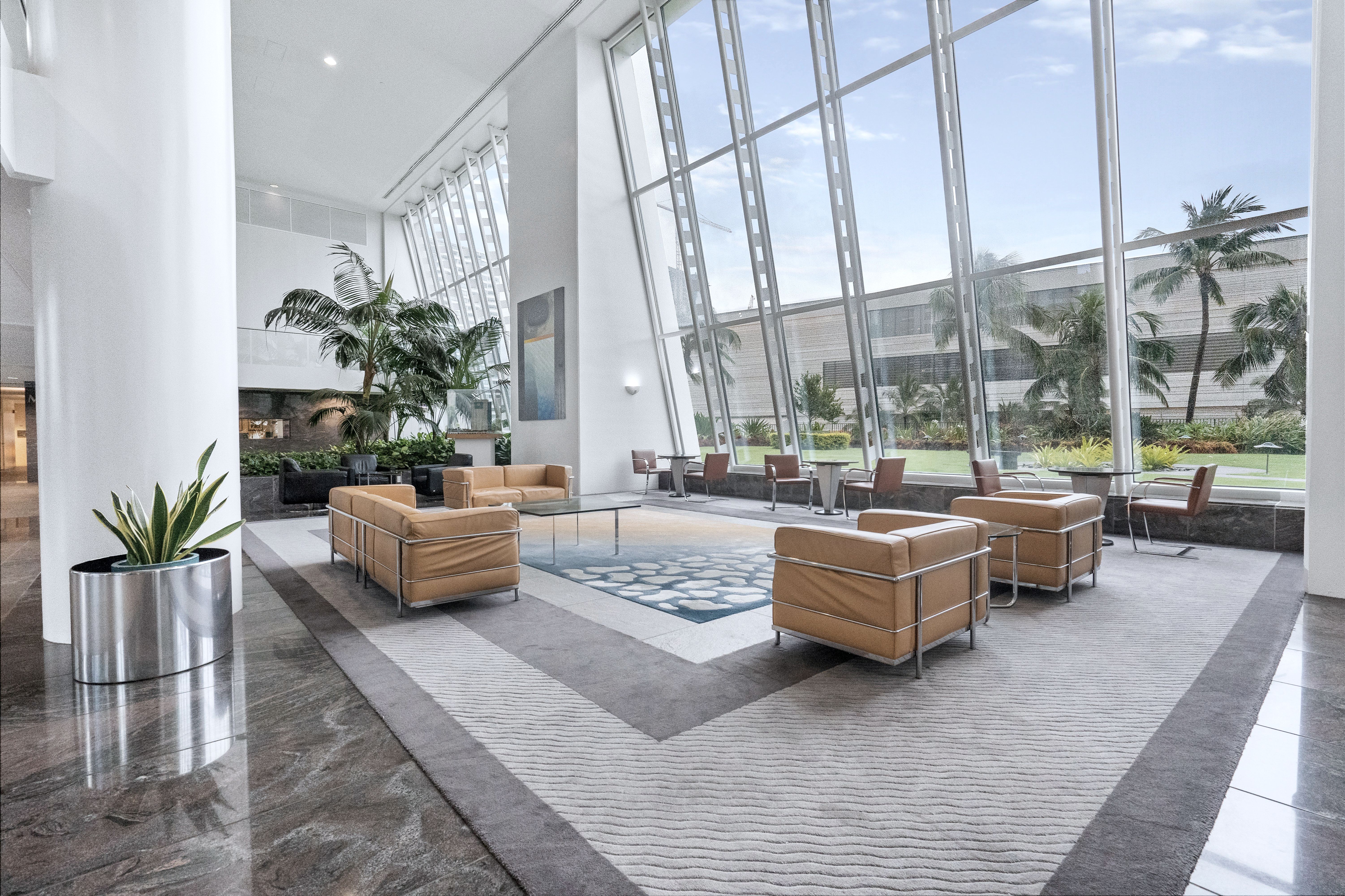 A tall lobby with planting inside and a glazed wall onto greenery.