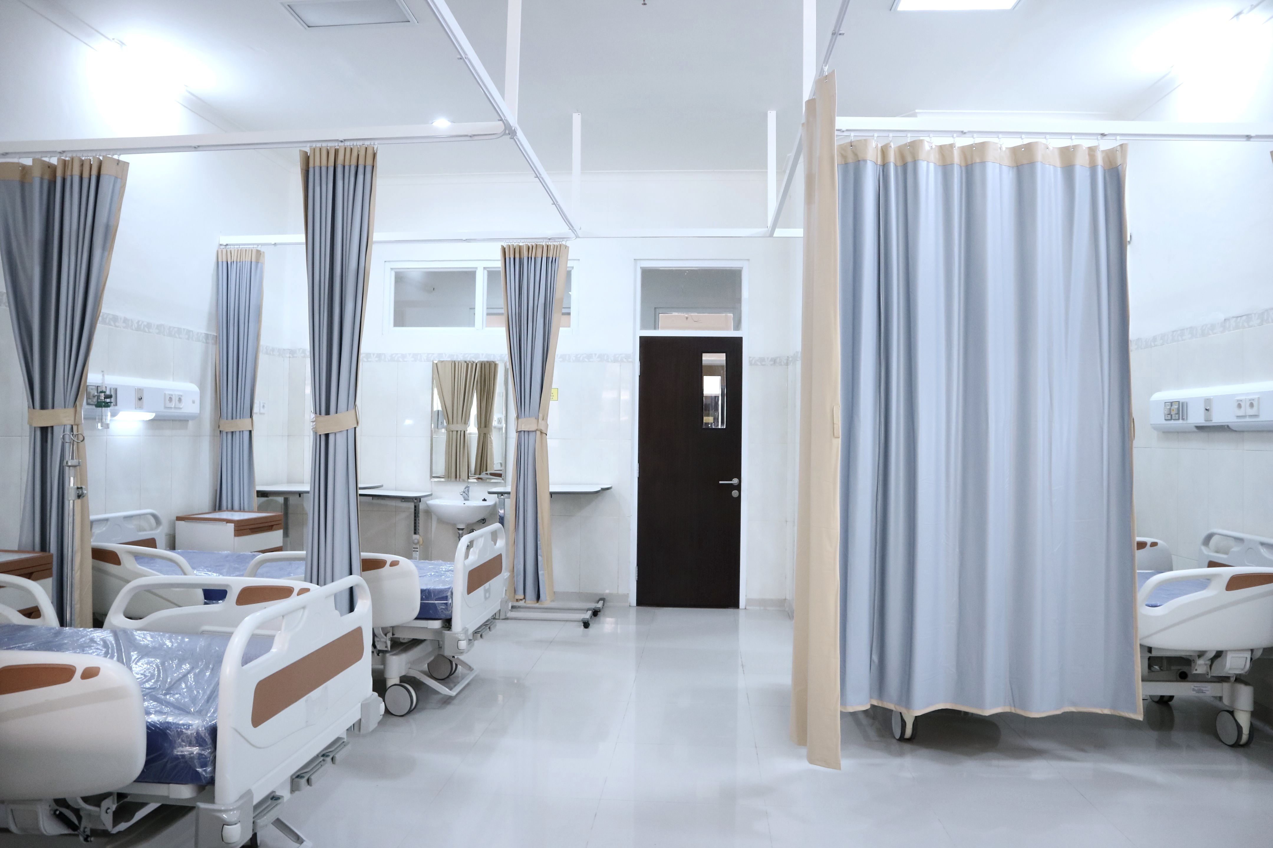 A multi-bed ward with beds on both sides and curtains drawn between them.