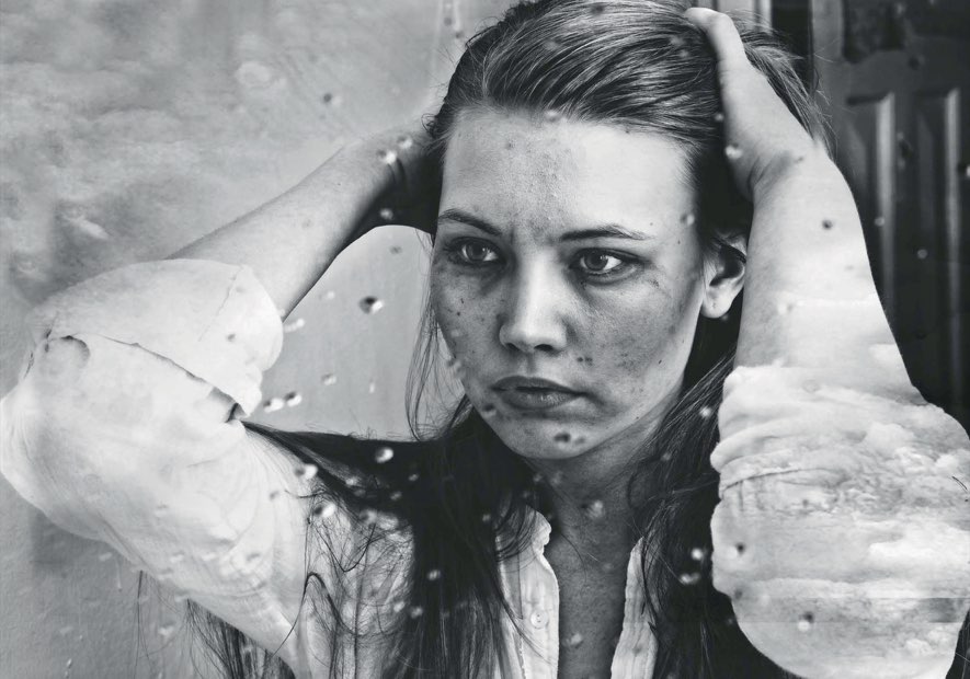A woman behind a rain-covered pane, her hands in her hair, in black and white